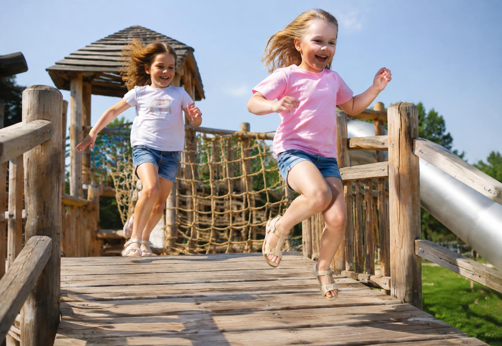 Two children leaping across a timber playground bridge